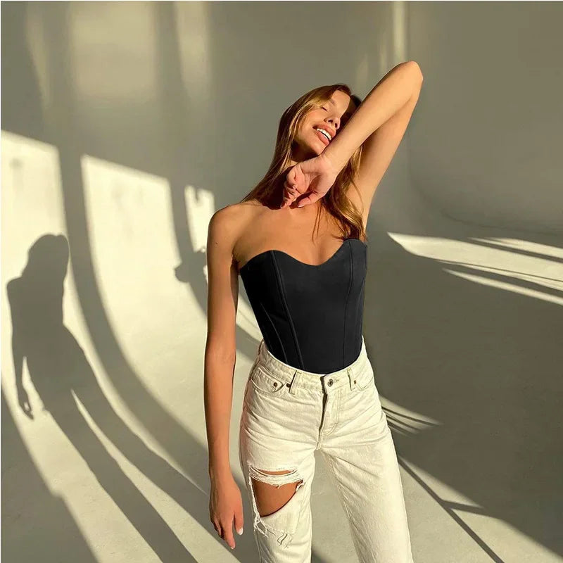 Woman in black strapless top and ripped white jeans, posing with sunlight shadows
