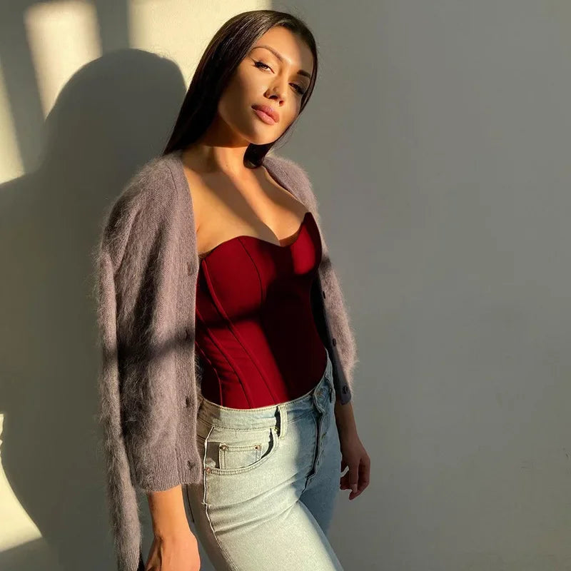 Woman in red corset top, gray cardigan, and light jeans, standing in sunlight